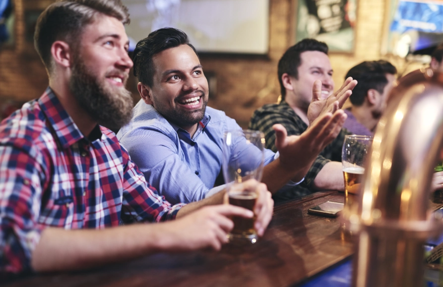 A group of men sitting at a bar with beers.