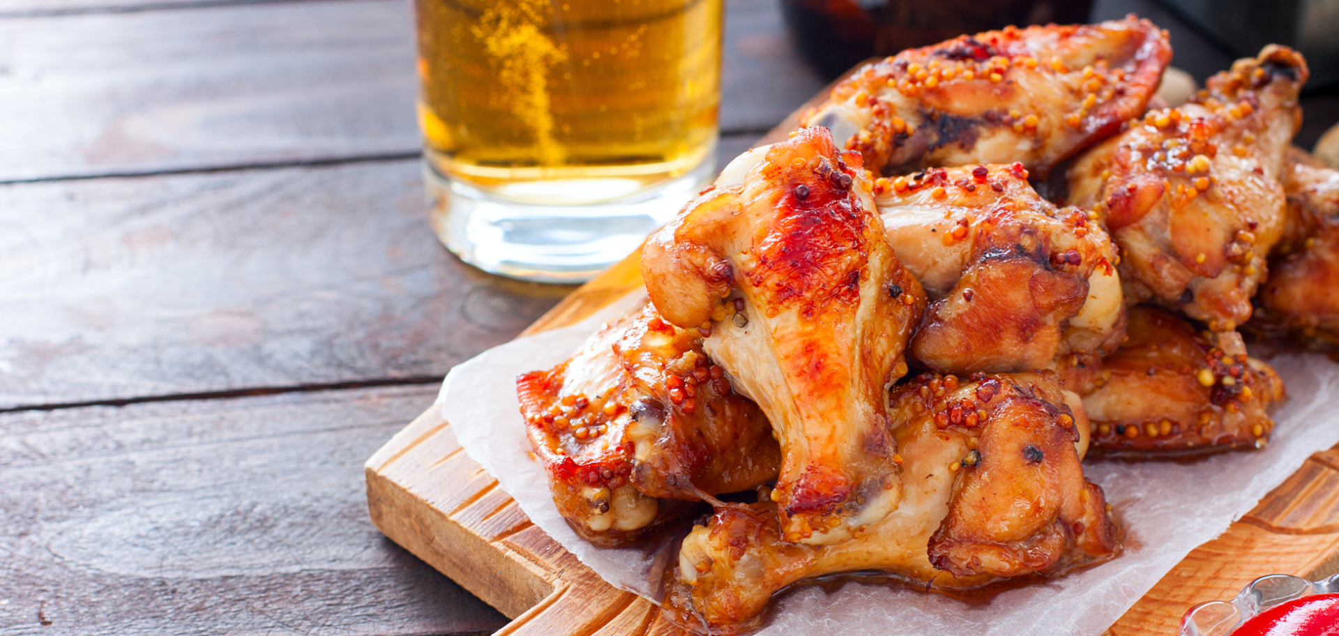 A wooden table with some chicken wings and a glass of beer